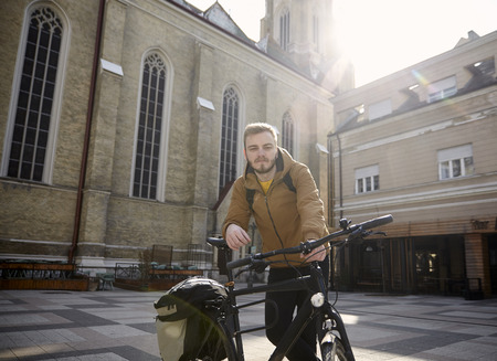 one young man, 20-29 years old, posing with his bicycle in a beautiful city square in Europe, Serbia, Novi Sad.の写真素材