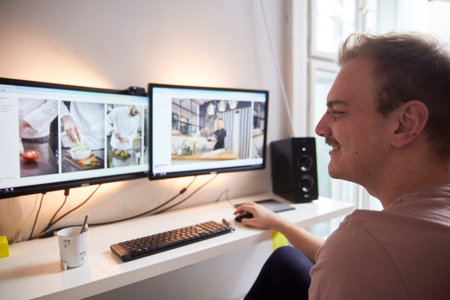 side view, one young mans head looking at two monitors in front of him. in his room. keyboard, mouse...