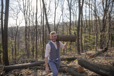 one young smiling man, dressed in suit, carrying wood log on his shoulder.の写真素材