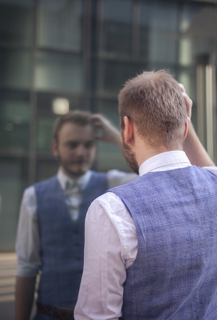 one young businessman, 20-29 years old, setting his hairstyle, touching his head looking at himself in a window mirror.の写真素材
