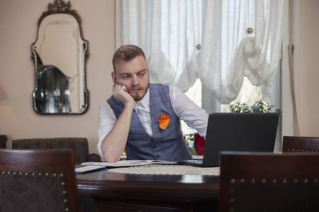 one young businessman, sitting in front of his computer, in his apartment room with antique furniture. bored of working, tired of problems.の写真素材