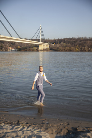one young smiling man, walking in river barefoot. Formal wear, wearing suit and shirt.の写真素材