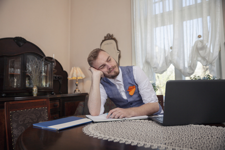 one young businessman, sitting in front of his computer, in his apartment room with antique furniture. bored of working, tired of problems.の写真素材