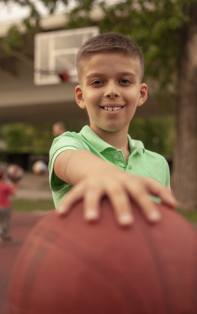 close-up of one nine years old boy, smiling to a camera, holding basketball ball in his hands.の写真素材