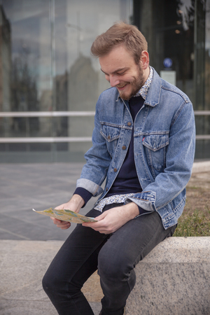 one young man, looking at a city map in his hands, outdoors.の写真素材