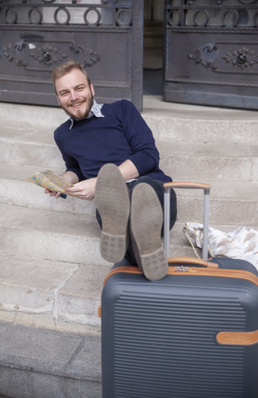 one young man, traveler or tourist, relaxing on a steps on a street. Looking at camera, while holding a city map.の写真素材