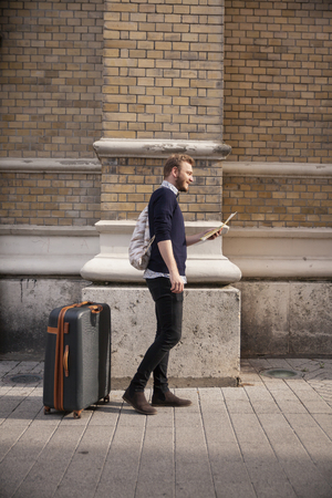 one young man - traveler or tourist, finding his way with a city map, on a narrow street outdoors. Behind is a old wall.の写真素材