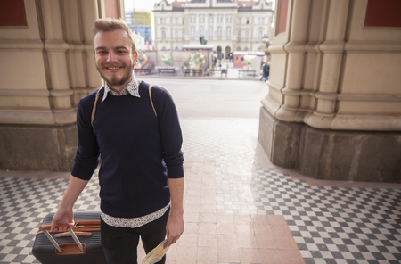 one young smiling man - traveler or tourist, walking with a suitcase and a city map. Old city European architecture outdoors.の写真素材