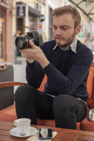 one young man, traveler or tourist, holding a DSLR camera,in his hands, while sitting in a cafe outdoors.の写真素材