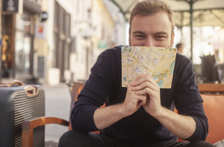 one young handsome man, smiling and happy, looking at a camera, holding a city map in his hands while covering his face. upper body shot, sitting in a cafe, on a street.の写真素材