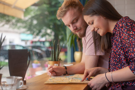 two friends sitting together in cafe, while searching on a city map.