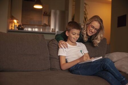 two people, young woman and boy, together happy, while doing homework in their living room.の写真素材