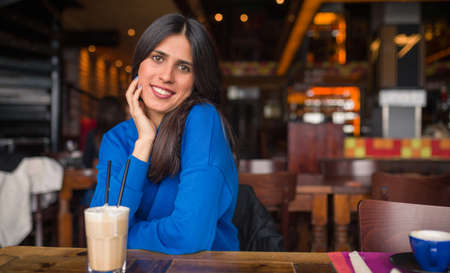 Portrait of pretty brunette in a cafe. Enjoying latte and looking at camera.の写真素材