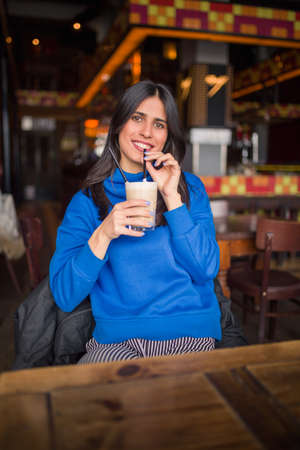 Portrait of pretty brunette in a cafe. Enjoying latte and looking at camera.の写真素材
