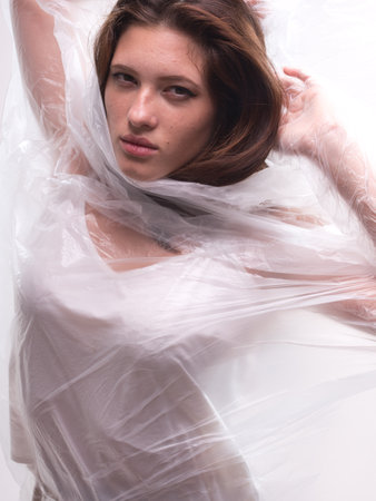 conceptual portrait, one young beautiful woman wraped in plastic sheet. Shot in studio, white background.の写真素材