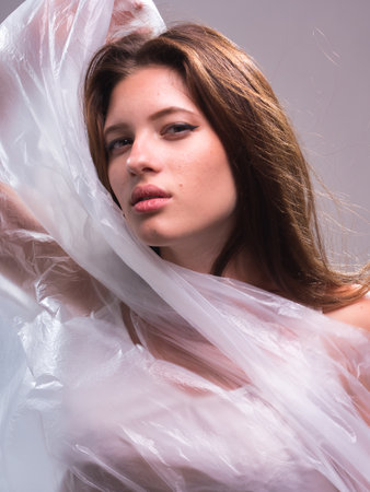 high key. Conceptual portrait with plastic sheets. One young woman strugling with plastic sheets.の写真素材