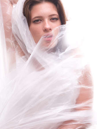 high key. Conceptual portrait with plastic sheets. One young woman strugling with plastic sheets.の写真素材