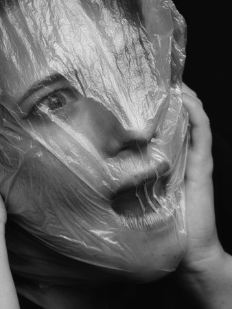 high key. Conceptual portrait with plastic sheets. One young woman strugling with plastic sheets.