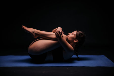 one young woman, exercising yoga, laying on a mat; calmly resting and streching in fetus position....