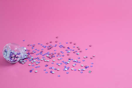 Lilac spangles are scattered from a bottle on a pink backgroundの写真素材