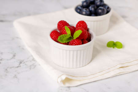 Raspberries and blueberries, mint leaves for breakfast on a white napkinの写真素材