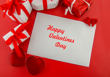 Valentine day concept. White letter paper with decorative hearts and a gift box with a greeting card for a holiday on a red background. Top view.の写真素材