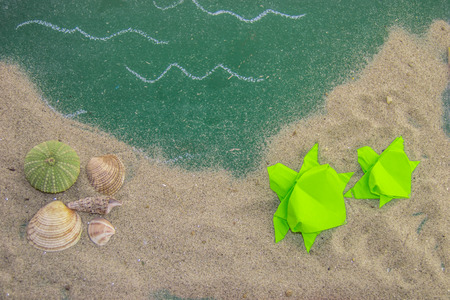 Paper origami turtles on the board for writing with shells on the sand.の写真素材