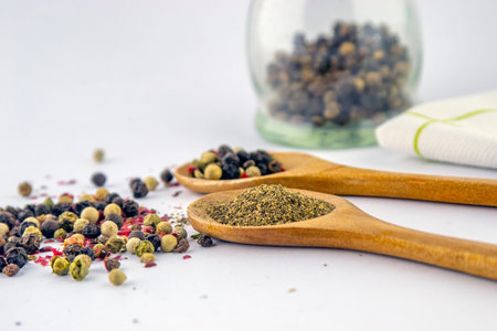 Colorful pepper in grain and ground black pepper in a wooden spoon on a white background