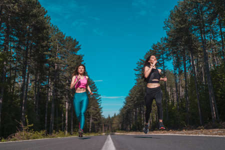 Fit sexy women competing each other, sprinting, jogging on country roadの写真素材
