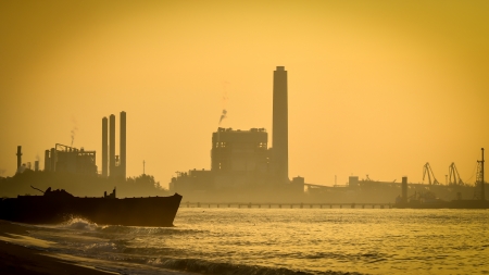 industrial plant silhouette at sunset and boat on beachのeditorial素材