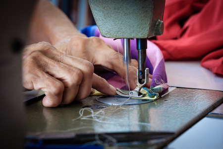 Woman's hands sewing fabric  repairs on old sewing machine.
Sewing process of the fabric pink. Old woman's hands behind sewing.の写真素材