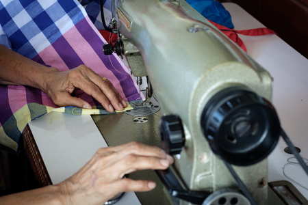 Woman's hands sewing fabric  repairs on old sewing machine.
Sewing process of the fabric pink. Old woman's hands behind sewing.の写真素材