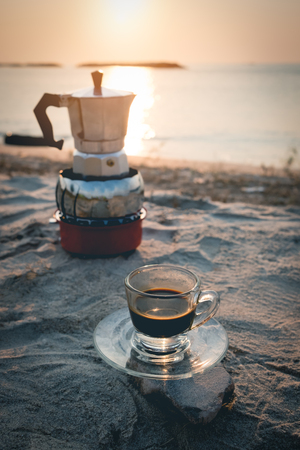 hot esspresso shot or hot black coffee from mokka pot  ready to serve at freshy morning time on the beach outdoor activity.black coffee ready to drink from mug on the beach outdoor picnic.の写真素材