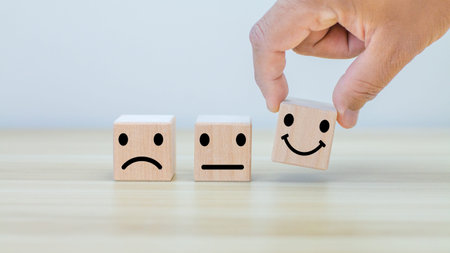 Hand putting smiley emotion to among normal and sad emotion which print screen on wooden cubic. Customer experience survey and satisfaction feedback concept.の写真素材