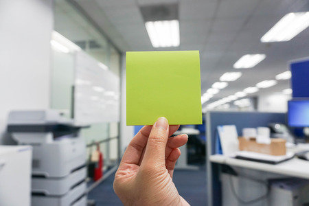 hold a green postit in hand with office backgroundの写真素材