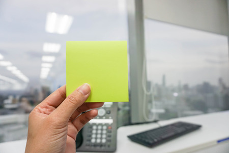 Hold a mockup green postit with office suppliers backgroundの写真素材