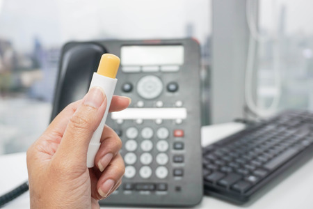 Hold a yellow lip balm with office backgroundの写真素材