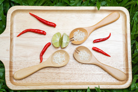 red chilli, lime and wooden spoon full of rice on the wooden tray placed on the green grassの写真素材