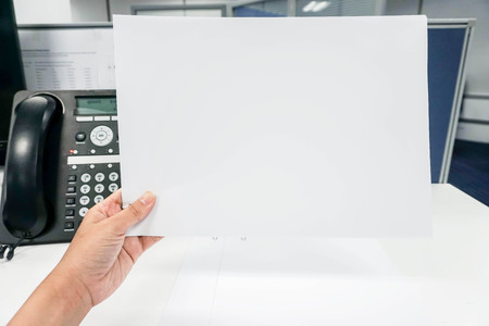 Hold mock up white paper sheet in hand with office backgroundの写真素材