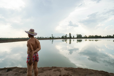 old man farmer with hat stand at the farm field near the river for agriculture planの写真素材