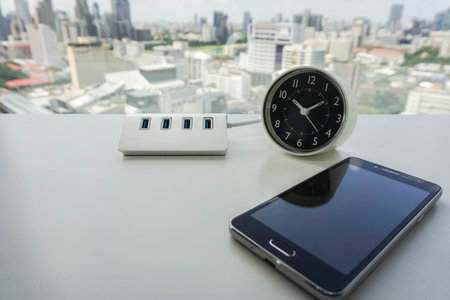 smartphone with USB hub and modern minimal clock on office desk