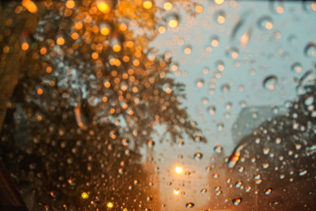 blurred raindrops with street light bokeh on car wind shield in the evening