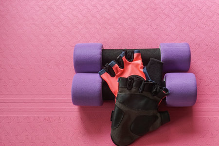 purple dumbbell with women fitness gloves on yoga mat for exercise