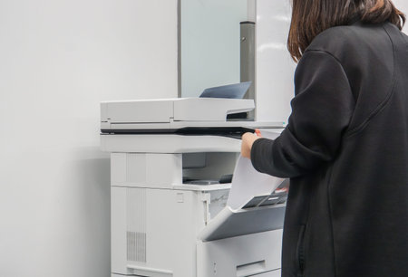 close up selective focus at businesswoman in black jacket put paper sheet into office printer tray...