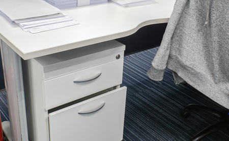 close up desk drawer and office desk with jacket on chairの写真素材