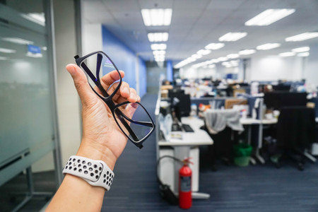 hold eye glasses with left hand with office workplace backgroundの写真素材