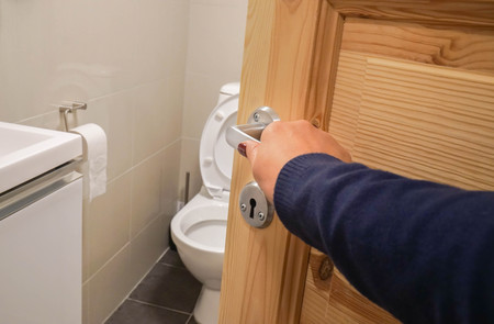close up woman hand with dark blue sweater open the toilet door handleの写真素材