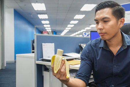 businessman eats fresh banana as light meal after work for dietのeditorial素材