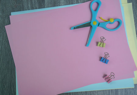flat lay blue scissors with paper clips and colorful papers for craft work