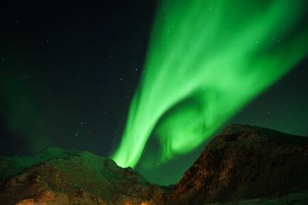 grainy green aurora northern light in the sky at mountain peak in Lofoten Islands with clear sky in winter seasonの写真素材